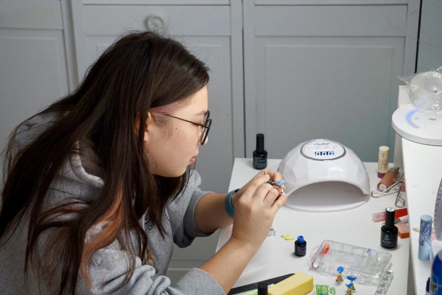 Destiny DoThanh ('20) paints the base coat of one of the ten press-on nails she's preparing for her customer's order. (Photo by Julia Dailard)
