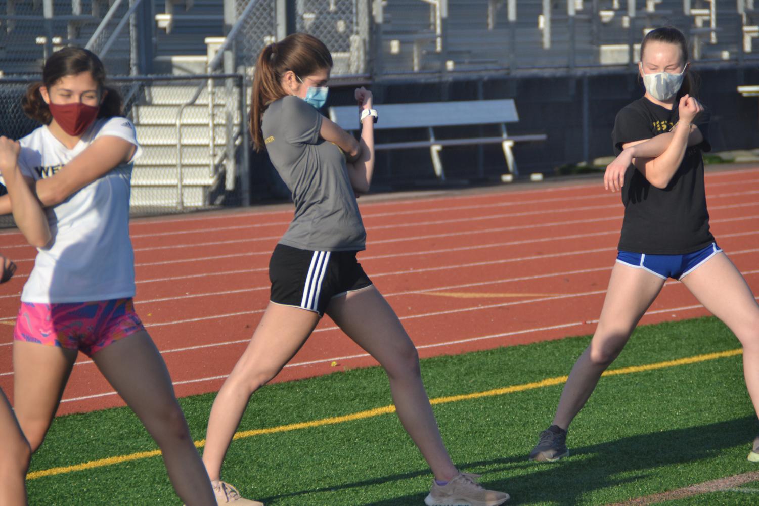 Maddie McFarland (11), Chloe Cartwright (12), and Milena Wilson (11) lead the stretches for the rest of the team. Photo by Matthew Flores