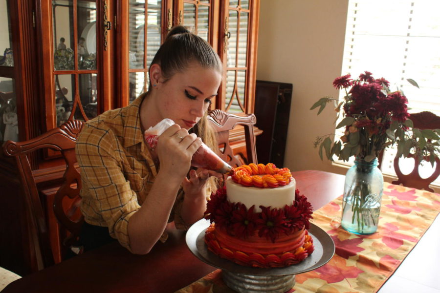 Jennifer Linnell (12) decorates a chocolate, fall-themed cake with vanilla frosting. As a part of her confectionary commissions, before completing any one of her cakes, she bakes each tier from scratch.