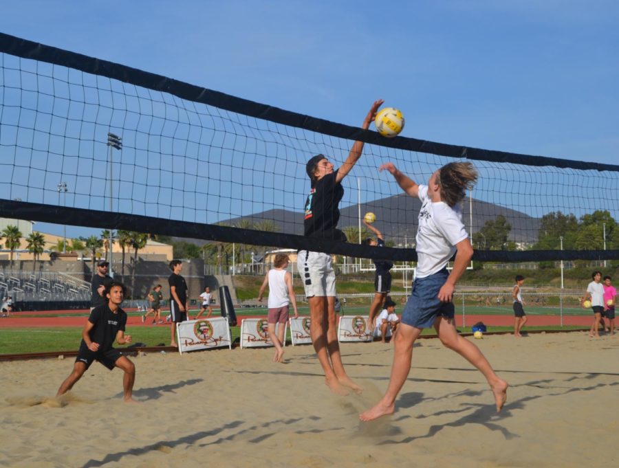 Luke Forster (12) blocks a spiked ball during beach volleyball practice while Marko Lipovic (12) gets ready to receive. Varsity members practice by playing king of the court with the junior varsity team to mentor the younger players. Photo by Jenna Ho-Sing-Loy.