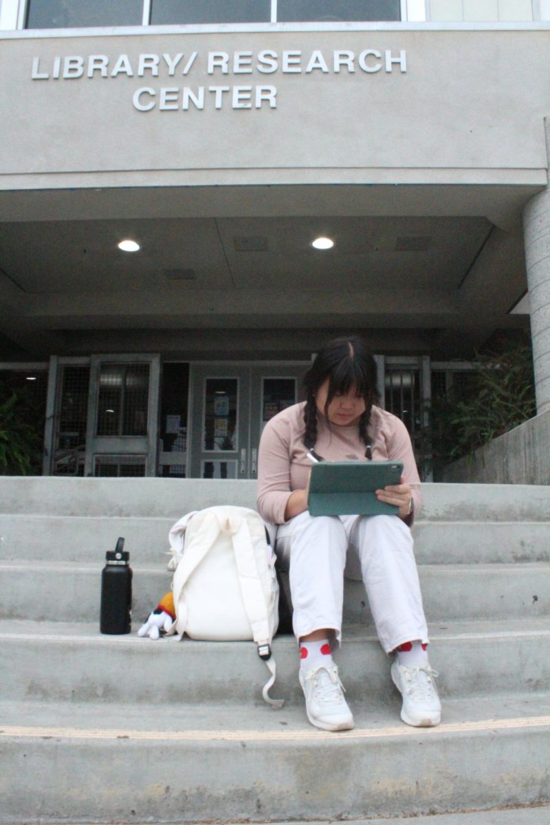 Woobin Wang (12) draws on her tablet outside the library, Oct. 16. Due to a lack of staffing and budget cuts, the library now closes at 4 p.m. Mondays. 