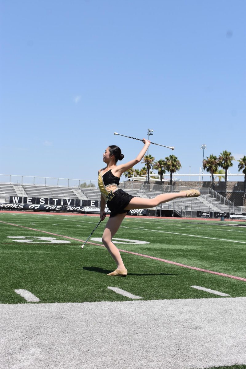 Chloe Ho (10) kicks back her left leg while in plié, raising a baton in the air, Aug 22. She completed her first baton twirling performance with Westview GOLD as the first baton twirler in Westview history. 