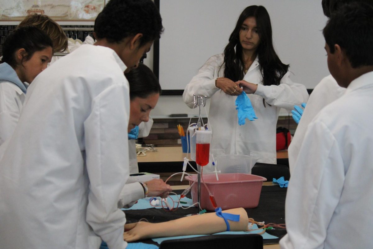 Biomed teacher Kelly Muench inserts a needle into a model arm as Amogh Hongal (9) and Sanvi Jain (9) observe, Sept. 25. This was Principles of Biomedical Science's first lab. 