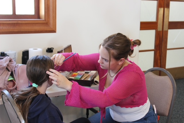 Elise Ball (10) paints flowers onto a. young girl's face at a carnival-themed event in a local synagogue. Ball has been face painting for three year, taking inspiration from the COVID-19 pandemic's makeup trends. 